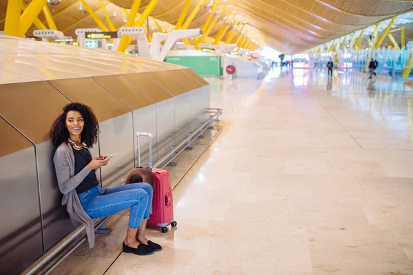 Jovem feliz ouvindo música com fones de ouvido e telefone celular no aeroporto — Fotografia de Stock