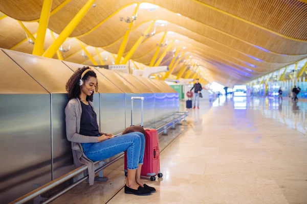 Glückliche junge Frau, die am Flughafen mit Kopfhörer und Handy Musik hört — Stockfoto