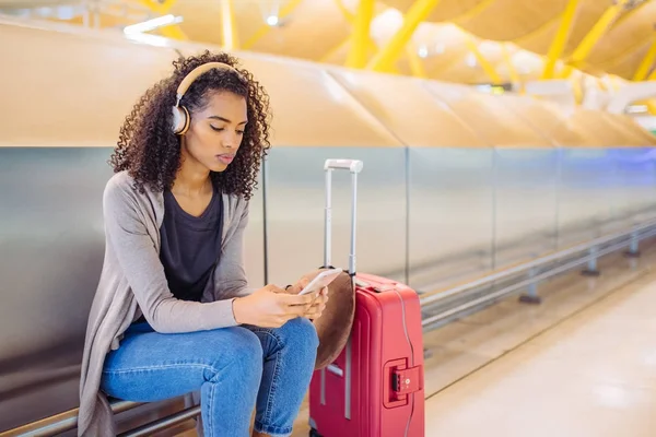 Glad ung kvinna lyssnar musik med hörlurar och mobiltelefon på flygplatsen — Stockfoto