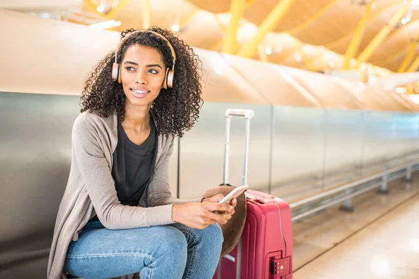 Glückliche junge Frau, die am Flughafen mit Kopfhörer und Handy Musik hört — Stockfoto