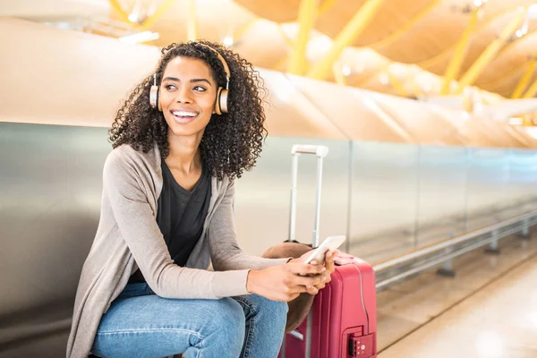 Glückliche junge Frau, die am Flughafen mit Kopfhörer und Handy Musik hört — Stockfoto