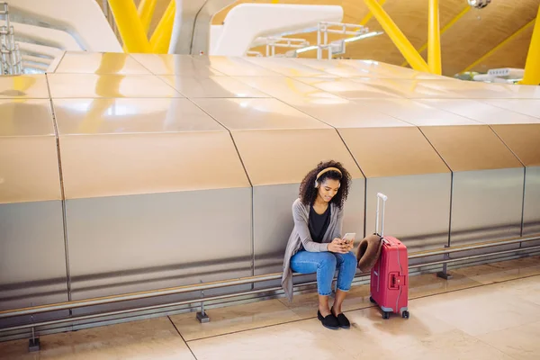 Szczęśliwa młoda kobieta słuchania muzyki z słuchawek i telefonu komórkowego na lotnisku — Zdjęcie stockowe