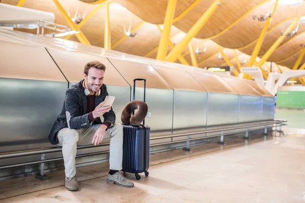 Junger Mann wartet mit Koffer am Flughafen und hört Musik — Stockfoto
