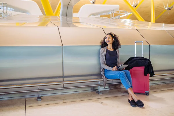 Frau am Flughafen benutzt Tablet und hört Musik über Kopfhörer — Stockfoto