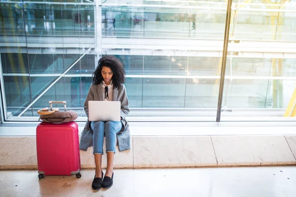 pencerenin önünde bekleyen Havaalanı'nda laptop ile çalışan siyah kadın 