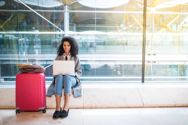 Mujer negra trabajando con el ordenador portátil en el aeropuerto esperando en la ventana — Foto de Stock