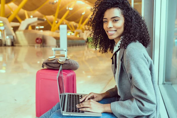 Mujer negra trabajando con el ordenador portátil en el aeropuerto esperando en la ventana — Foto de Stock
