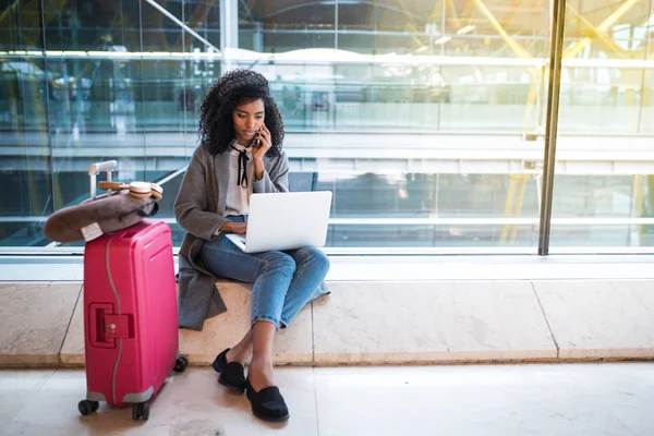 Kobieta przy użyciu telefonu komórkowego i laptopa na lotnisku siedząc przy oknie — Zdjęcie stockowe