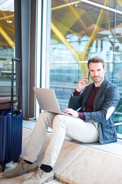 남자는 창 옆에 있는 노트북과 휴대 전화를 사용 하 여 공항에 앉아. — 스톡 사진