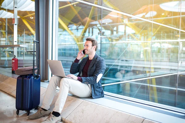 Hombre sentado en el aeropuerto con portátil y teléfono móvil al lado de la ventana . — Foto de Stock