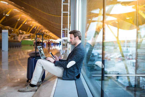 ウィンドウの横にノート パソコンと携帯電話を使用して空港に座っている男の人. — ストック写真