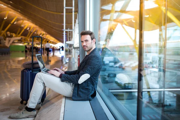 dizüstü bilgisayar ve cep telefonu yanında penceresini kullanarak Havaalanı'nda oturan adam.