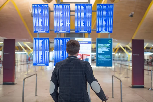 Człowiek ogląda panelu informacje harmonogramu na lotnisku z walizką — Zdjęcie stockowe