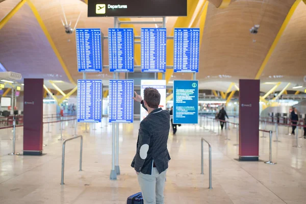 男がスーツケースを持って空港の時刻表情報パネルを見て — ストック写真