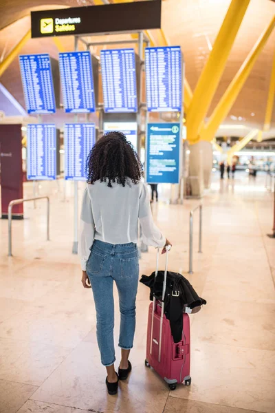 Donna che guarda il pannello di informazioni sugli orari in aeroporto con una valigia — Foto Stock
