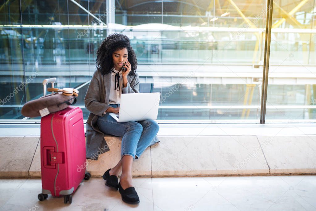 woman using mobile phone and laptop at the airport sitting at the window