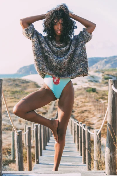Giovane donna nera che fa yoga in un ponte pedonale in legno vicino al mare — Foto Stock