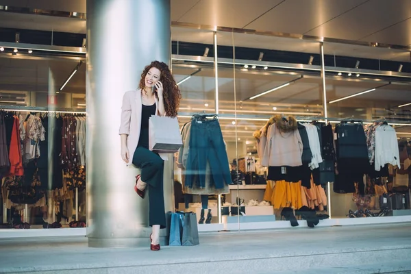 Ευτυχής όμορφη νεαρή κοκκινομάλλα γυναίκα κάνει ψώνια και μιλώντας στο κινητό τηλέφωνο — Φωτογραφία Αρχείου