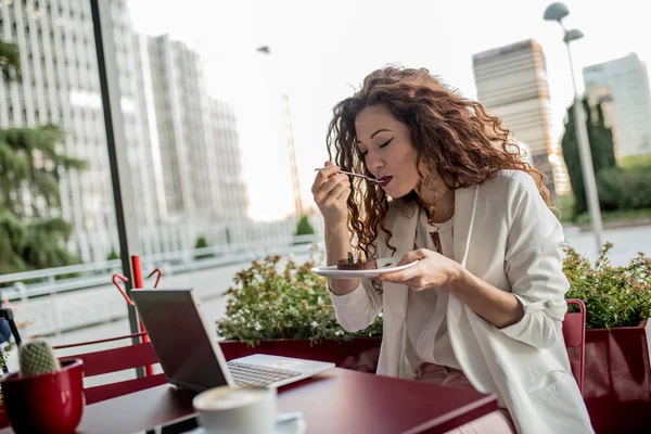 Молодая деловая рыжая женщина за компьютером и ест торт — стоковое фото