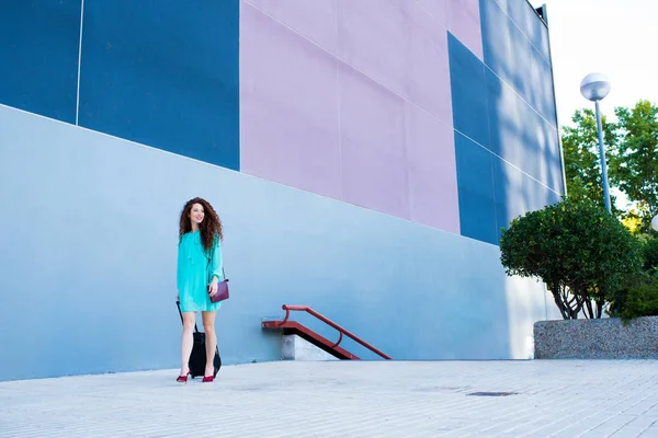Glücklich schöne junge rothaarige Frau mit einem Koffer, der an einer bunten Wand vorbeiläuft — Stockfoto