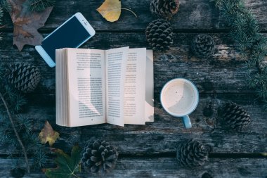 Kitap ve kahve ve çam ağaçları açık ahşap bir masa üstünde hareket eden telefon