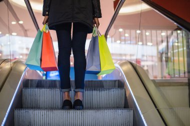 Kadın bacakları ile renkli alışveriş torbaları üzerinde bir alışveriş alışveriş merkezinde yürüyen merdiven