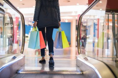 Kadın bacakları ile renkli alışveriş torbaları üzerinde bir alışveriş alışveriş merkezinde yürüyen merdiven