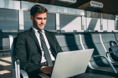Çantayı bilgisayarla havaalanında uçuş için bekleyen oturan genç iş adamı