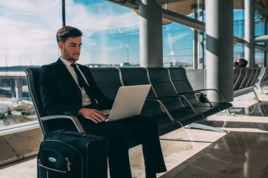 Çantayı bilgisayarla havaalanında uçuş için bekleyen oturan genç iş adamı