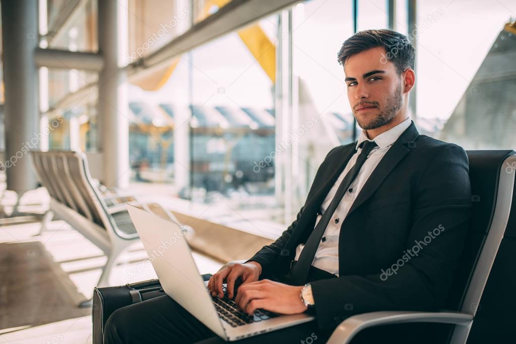 Young business man sitting on the computer with the suitcase at the airport waiting for the flight