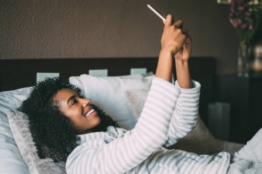 gülümseyen ve uzağa yatak arayan telefon kullanarak kıvırcık saçlı oldukça siyah bir kadın yakın çekim