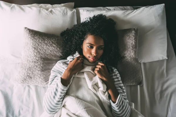 Hermosa mujer negra pensativa con el pelo rizado acostado en la cama mirando hacia otro lado — Foto de Stock