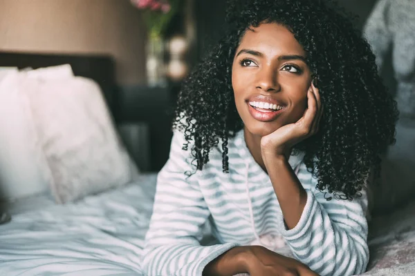 Κοντινό πλάνο του μια όμορφη μαύρη γυναίκα με σγουρά μαλλιά χαμογελώντας και ξαπλωμένος στο κρεβάτι που βλέπει μακριά — Φωτογραφία Αρχείου