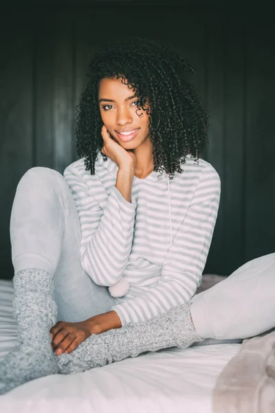 Primo piano di una bella donna nera con i capelli ricci sorridenti sedersi sul letto a guardare la fotocamera — Foto Stock