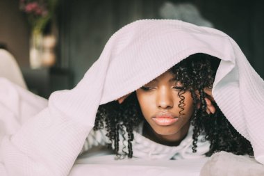 Kafasını yatakta levha ile kapsayan güzel ciddi düşünceli ve üzgün siyah kadın