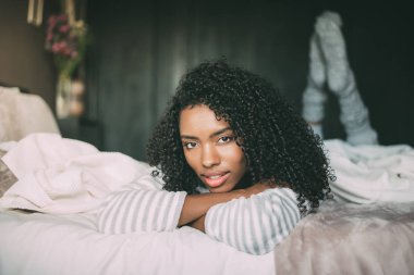 gülümseyen ve kameraya bakarak yatakta yatan kıvırcık saçlı oldukça siyah bir kadın yakın çekim