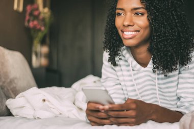 gülümseyen ve uzağa yatak arayan telefon kullanarak kıvırcık saçlı oldukça siyah bir kadın yakın çekim