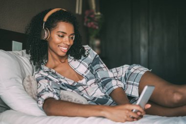 kadını yatağa akıllı telefon ve kulaklık ile müzik dinleme