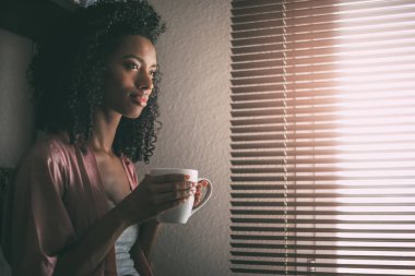 fincan kahve ile pencerenin önünde oturan oldukça siyah kadın