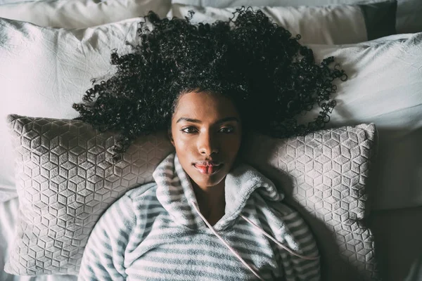 Όμορφη μαύρη γυναίκα με σγουρά μαλλιά ξαπλωμένος στο κρεβάτι, βλέπουν τα φωτογραφικών μηχανών — Φωτογραφία Αρχείου