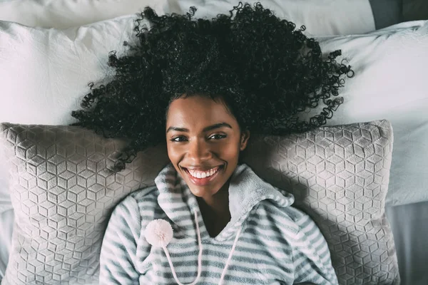Όμορφη μαύρη γυναίκα με σγουρά μαλλιά χαμογελώντας και ξαπλωμένος στο κρεβάτι, βλέπουν τα φωτογραφικών μηχανών — Φωτογραφία Αρχείου