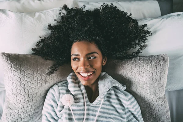 Όμορφη μαύρη γυναίκα ξαπλωμένη στο κρεβάτι, βλέπουν τα φωτογραφικών μηχανών χαμογελώντας — Φωτογραφία Αρχείου