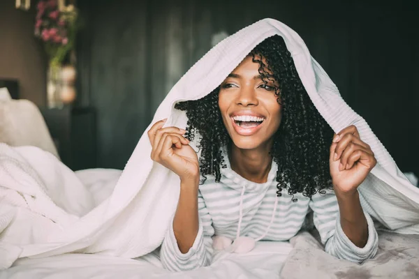 Κοντινό πλάνο του μια όμορφη μαύρη γυναίκα με σγουρά μαλλιά χαμογελώντας και καλύπτουν με φύλλα στο κρεβάτι που βλέπει μακριά — Φωτογραφία Αρχείου