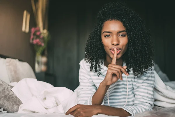 attractive black woman asking for silence with finger on lips on bed