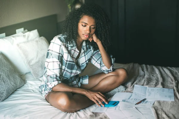 worried black woman with bills and finance problems on bed