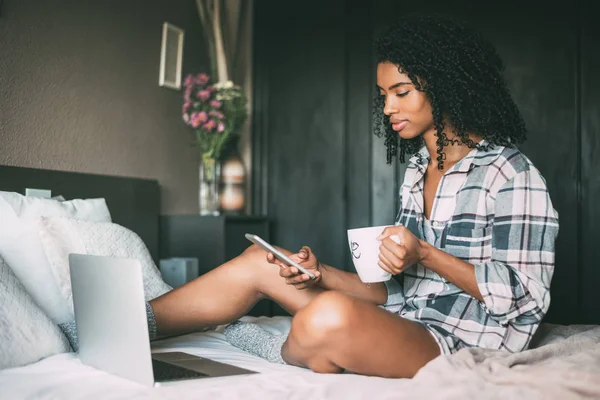 Krásná černá žena na lůžku s notebookem a šálek kávy — Stock fotografie