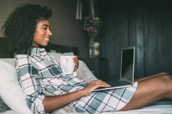 Krásná černá žena na lůžku s notebookem a šálek kávy — Stock fotografie