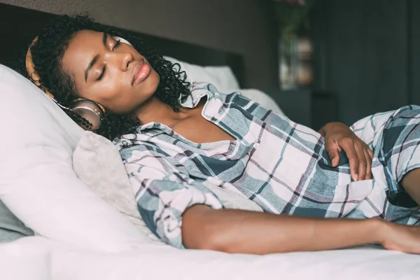 Donna che dorme sul letto e ascolta musica con cuffie e smartphone — Foto Stock