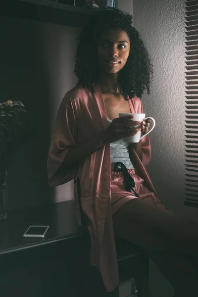 Όμορφη μαύρη γυναίκα κάθεται στο παράθυρο με φλιτζάνι καφέ — Φωτογραφία Αρχείου
