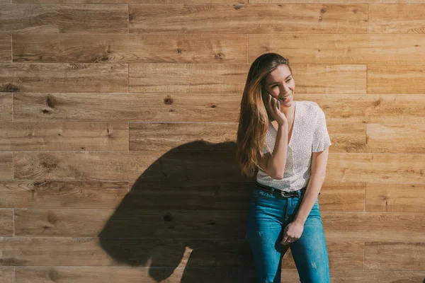 木製の壁でスマート フォンを使用して幸せな女 — ストック写真